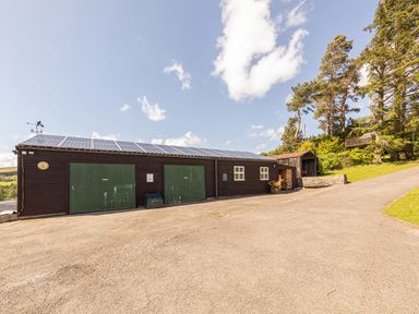 A building with green doors and solar panels on the roof next to a paved driveway and trees at Heatherbrae in Middleton-In-Teesdale