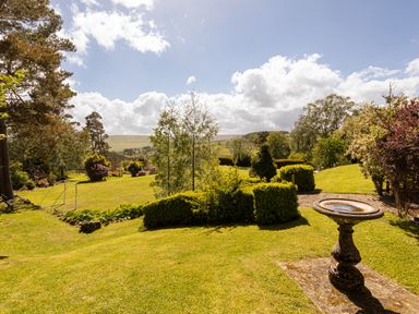 A garden with a birdbath trimmed hedges and trees with hills in the background at Heatherbrae in Middleton-In-Teesdale