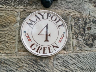 A ceramic house number plaque with the number 4 and text Maypole Green mounted on a stone wall at 4 Maypole Green in Fylingthorpe