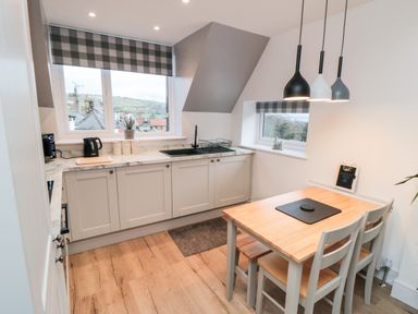 A kitchen with cabinets a sink a wooden dining table and chairs with pendant lights at 4 Maypole Green in Fylingthorpe