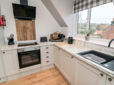 A kitchen with a stove oven microwave toaster kettle and sink by a window at 4 Maypole Green in Fylingthorpe