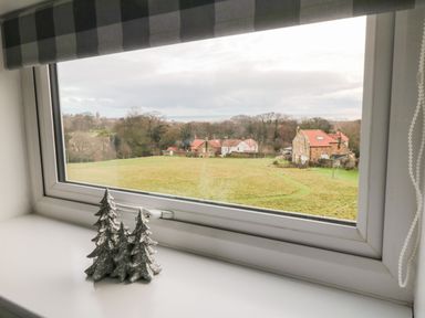 A window with a silver decorative item shaped like three trees on the sill and a view of houses and fields at 4 Maypole Green in Fylingthorpe