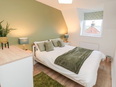 A bedroom with a double bed green pillows and blanket bedside tables with lamps a chest of drawers and a window at 4 Maypole Green in Fylingthorpe