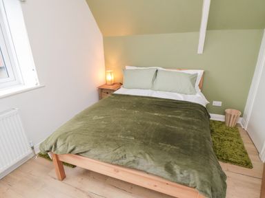 A bedroom with a bed with green bedding a wooden bedside table with a lamp a window and a green rug at 4 Maypole Green in Fylingthorpe