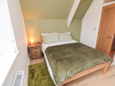 A bedroom with a wooden double bed green bedding a wooden bedside table with a lamp a green rug and a wooden door at 4 Maypole Green in Fylingthorpe