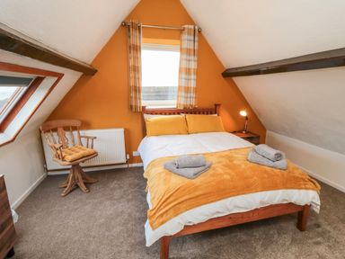 A bedroom with a double bed yellow pillows and blanket wooden chair and bedside table with lamp at 4 Maypole Green in Fylingthorpe