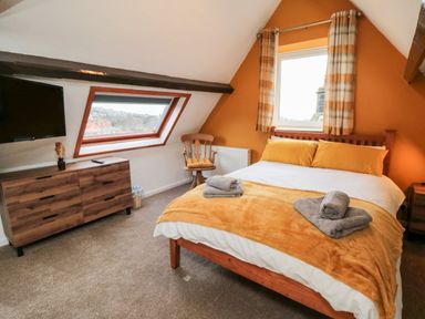 A bedroom with a bed orange bedding a wooden dresser a chair and a window at 4 Maypole Green in Fylingthorpe