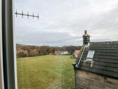 A view of a grassy field with houses and trees beyond from a window at 4 Maypole Green in Fylingthorpe