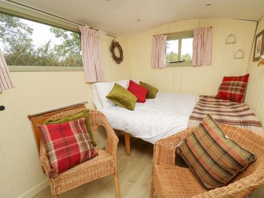 A small room with a bed and two wicker chairs with cushions at Tilly Gypsy-style Caravan Hut in Llangorse