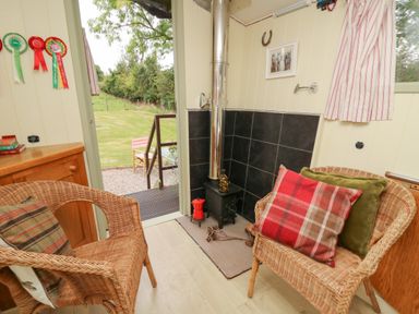 A small sitting area with wicker chairs and a wood stove with a chimney pipe at Tilly Gypsy-style Caravan Hut in Llangorse