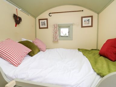 A bed with striped and solid pillows near a small window with curtains in a room at Sweet Briar Shepherds Hut in Llangorse