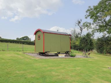 A small green and red shepherds hut on wheels in a grassy field with a table and two chairs nearby at Sweet Briar Shepherds Hut in Llangorse