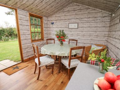 A dining area with a round table covered by a tablecloth surrounded by four chairs and a wicker armchair at Sweet Briar Shepherds Hut in Llangorse