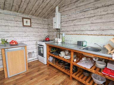 A kitchen with wooden shelves holding dishes and cookware a stove a mini fridge and a sink at Sweet Briar Shepherds Hut in Llangorse