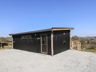 A black building with a door and small windows on a gravel area with countryside in the background at Bryn Hafod in Llandrindod Wells