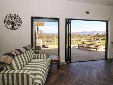 A living room with a striped sofa next to glass doors opening onto a wooden deck with a picnic table at Bryn Hafod in Llandrindod Wells