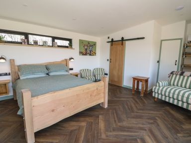 A bedroom with a wooden bed, striped chairs, a striped sofa, wooden tables, and a sliding wooden door at Bryn Hafod in Llandrindod Wells