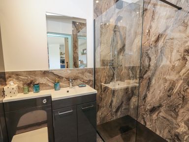 A bathroom with a sink and soap dispenser next to a glass shower with marble walls at Bryn Hafod in Llandrindod Wells