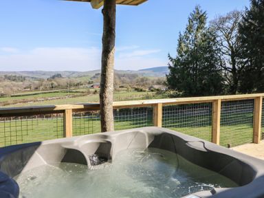 A hot tub on a wooden deck overlooking green fields and hills at Bryn Hafod in Llandrindod Wells