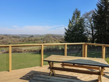 A wooden deck with a picnic table and a view of fields and trees at Bryn Hafod in Llandrindod Wells