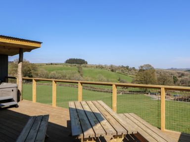 A wooden deck with picnic table and railing overlooking green fields and hills at Bryn Hafod in Llandrindod Wells