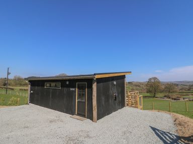 A black building with a door and window on a gravel area in a rural setting at Llety Cariad in Llandrindod Wells
