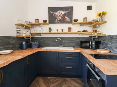 A kitchen with wooden countertops blue cabinets open shelves and a painting of a cow at Llety Cariad in Llandrindod Wells
