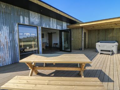 An outdoor wooden deck with picnic table and hot tub beside a building with corrugated metal and wooden walls at Llety Cariad in Llandrindod Wells