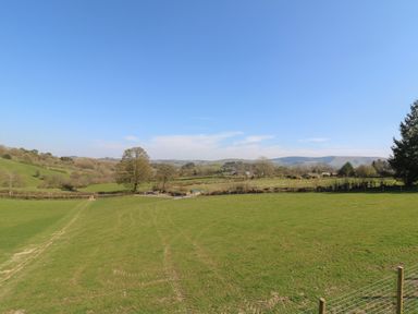 A wide green field with trees and hills under a clear blue sky at Llety Cariad in Llandrindod Wells