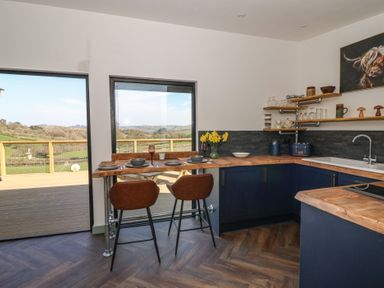 A kitchen with wooden countertops, blue cabinets, bar stools, and a view of the countryside at Llety Cariad in Llandrindod Wells