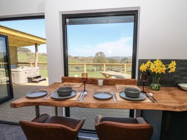A dining table set with plates bowls glasses and cutlery next to a window with a view of a deck and countryside at Llety Cariad in Llandrindod Wells