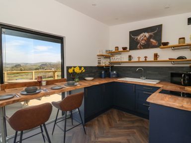 A kitchen with wooden countertops brown chairs and a window with a view of hills at Llety Cariad in Llandrindod Wells