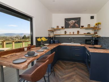 A kitchen with wooden countertops and shelves with table set by a window showing a view of greenery at Llety Cariad in Llandrindod Wells