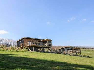 Two wooden cabins on stilts with balconies on a grassy hillside under a clear sky at Llety Cariad in Llandrindod Wells
