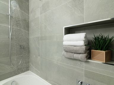 A bathroom with a shower head and towels stacked on a shelf at Sandy Cove in Praa Sands