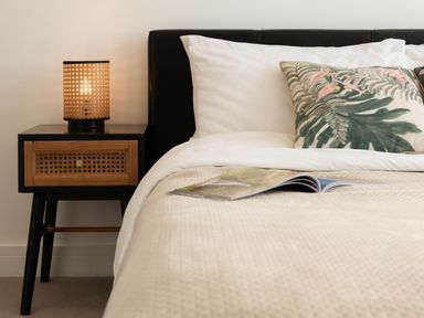A bedroom with a bed, nightstand, lamp, and magazine at Sandy Cove in Praa Sands