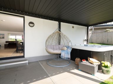An outdoor patio with a hanging chair and hot tub at Sandy Cove in Praa Sands