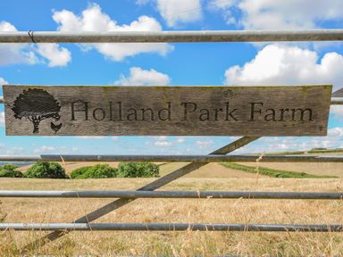 A wooden sign on a metal gate with fields and trees in the background at Holland Park Farm
