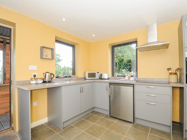 A kitchen with yellow walls gray cabinets a kettle microwave toaster and silver fridge at Lillemor in South Tawton near Whiddon Down