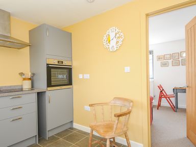 A kitchen with grey cabinets oven and a wooden chair next to a yellow wall with a clock at Lillemor South Tawton near Whiddon Down
