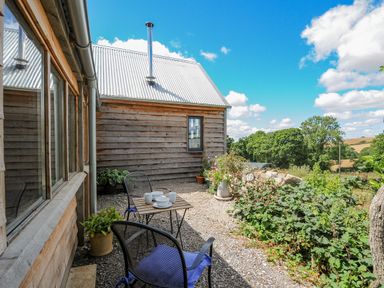 An outdoor patio area with a small table set and two chairs beside a wooden building at Lillemor in South Tawton near Whiddon Down
