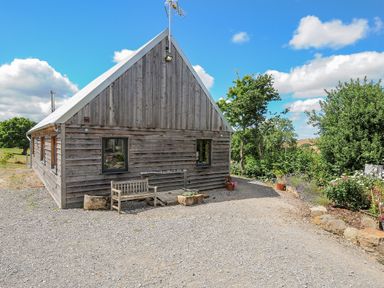 A wooden house with a bench and flower pots outside surrounded by trees and gravel at Lillemor in South Tawton near Whiddon Down