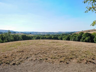 A dry grassy field with trees and hills in the distance at Lillemor South Tawton near Whiddon Down