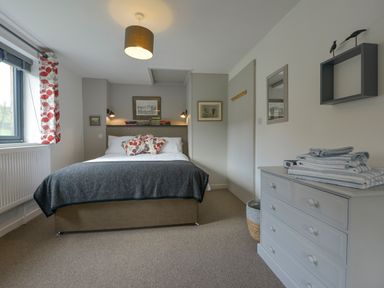A bedroom with a bed and pillows next to a window and a chest of drawers with folded towels at Lillemor South Tawton near Whiddon Down