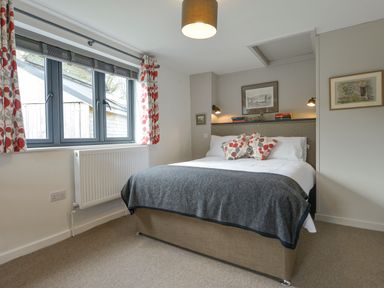 A bedroom with a double bed pillows and a blanket next to a window with patterned curtains at Lillemor in South Tawton near Whiddon Down