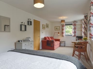 A room with a bed, a chest of drawers, a red sofa, a dining table with chairs, and curtains at Lillemor in South Tawton near Whiddon Down