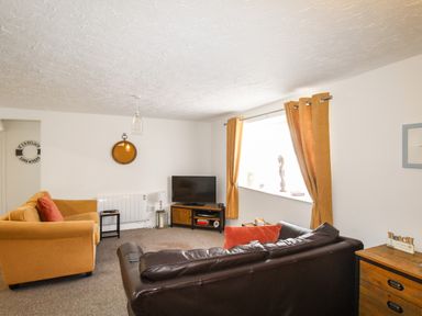 A living room with a brown leather sofa and orange upholstered armchair near a window with orange curtains at Brewers Retreat in Weymouth