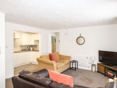 A living room with sofas and a TV cabinet next to an open kitchen at Brewers Retreat in Weymouth