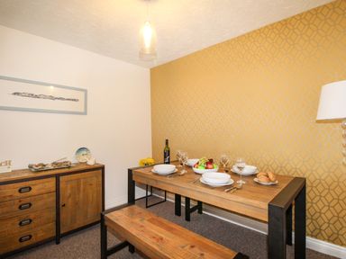 A dining room with a wooden table, bench seating, sideboard, patterned yellow wallpaper and table set with dishes and fruit at Brewers Retreat in Weymouth