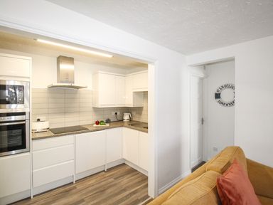 A kitchen with white cabinets and appliances next to a living area with a yellow sofa and a pillow at Brewers Retreat in Weymouth